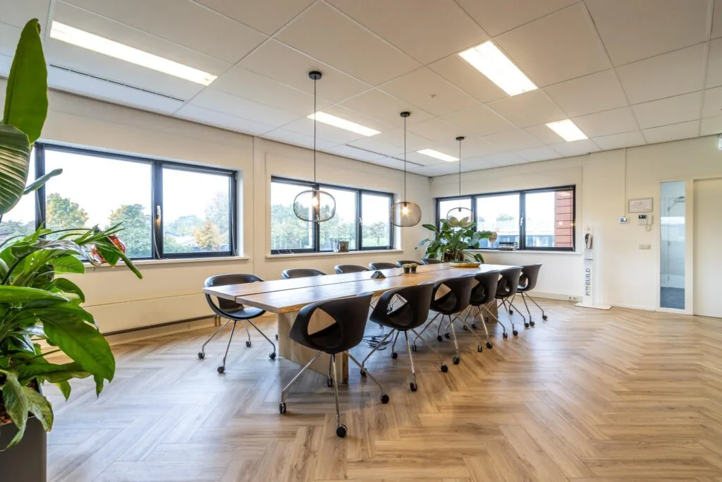 Moderne vergaderruimte aan de Lage Biezenweg met lange houten tafel, zwarte stoelen, grote ramen en hanglampen.